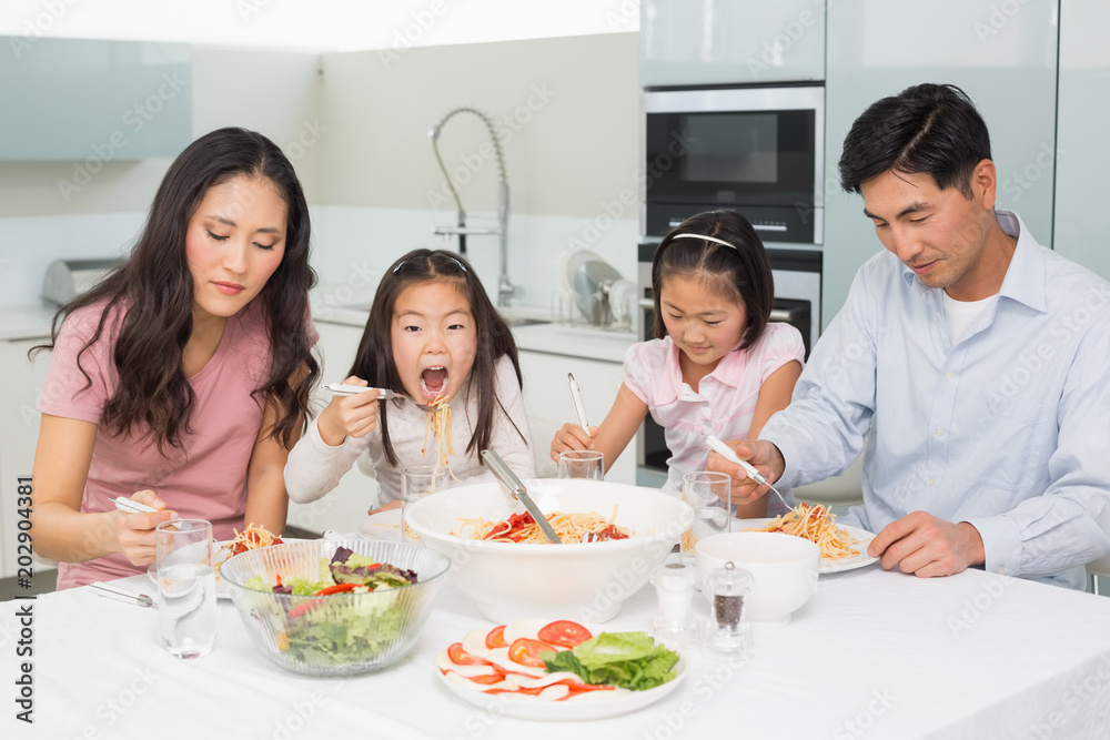 Happy family of four enjoying spaghetti lunch in kitchen Happy family of four enjoying spaghetti lunch in kitchen
