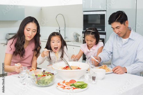 Happy family of four enjoying spaghetti lunch in kitchen