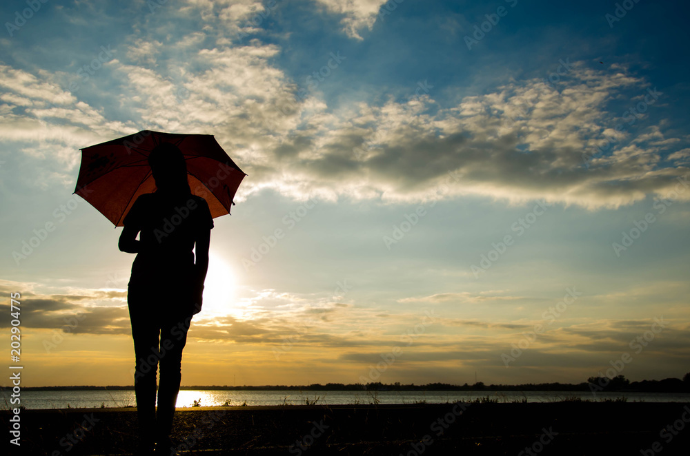 Silhouette of a woman standing holding an umbrella in the evening alone with loneliness.