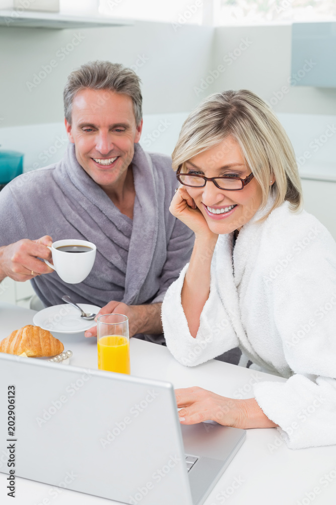 Couple in bathrobes with coffee and juice using laptop