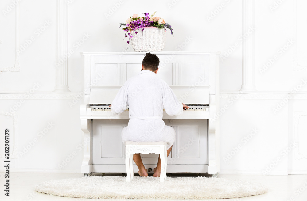 Man in bathrobe enjoys morning while playing piano. Talented musician concept. Man sleepy in bathrobe sit in front of piano musical instrument in white interior on background, rear view. Man in bathrobe enjoys morning while playing piano. Talented musician concept. Man sleepy in bathrobe sit in front of piano musical instrument in white interior on background, rear view.