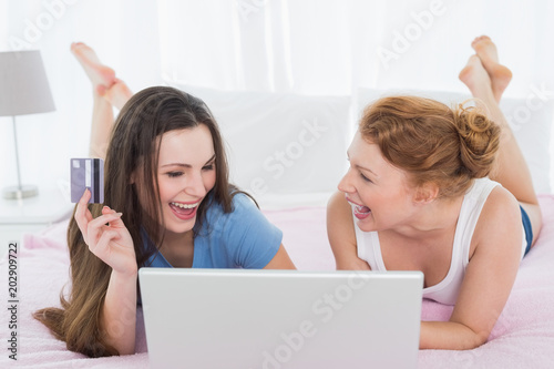 Cheerful female friends doing online shopping in bed