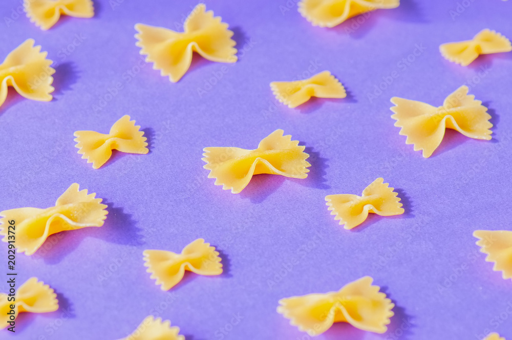 Different size of farfalle pasta on a violet background. Different size of farfalle pasta on a violet background.