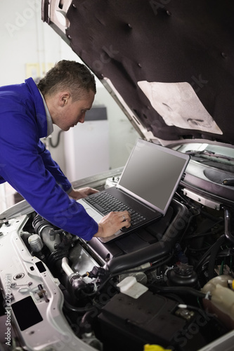 Mechanic looking at a computer on a car engine © WavebreakmediaMicro