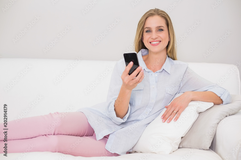 Happy casual blonde relaxing on couch holding smartphone Happy casual blonde relaxing on couch holding smartphone