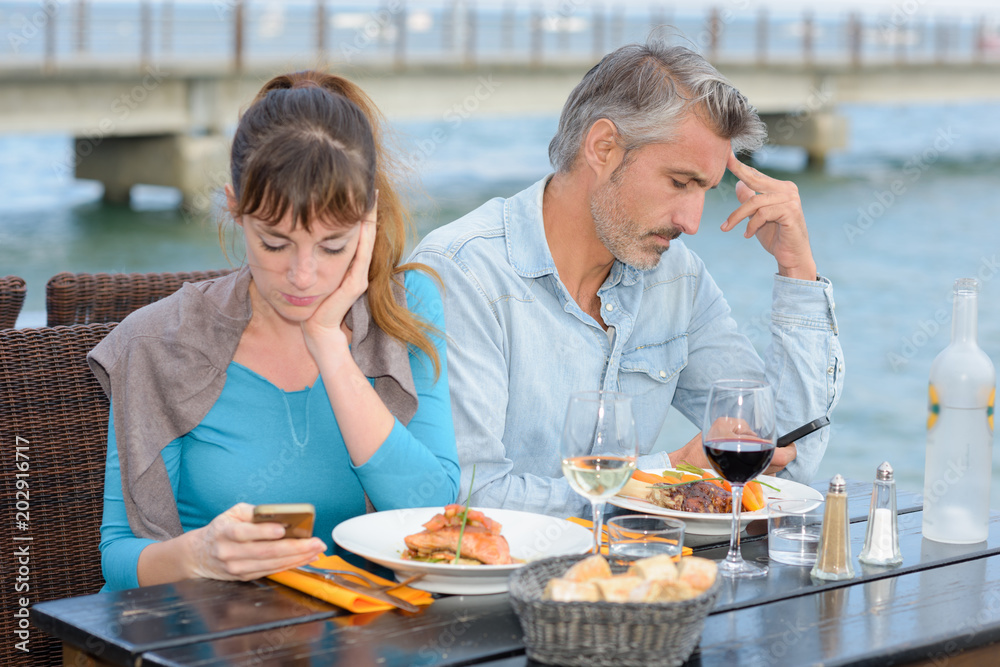 Couple having meal both preoccupied with cellphones Couple having meal both preoccupied with cellphones