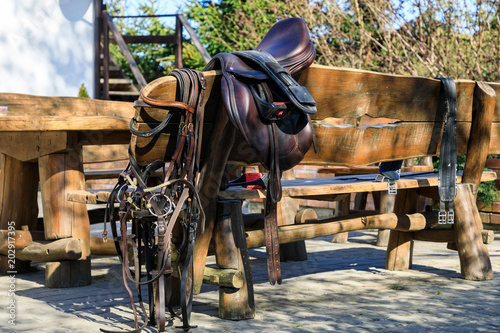 Horseback equipment are hanging on the wooden chair outdoors