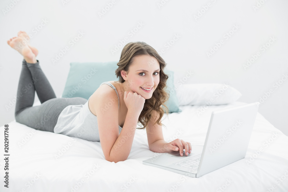 Smiling casual brunette using laptop in bed Smiling casual brunette using laptop in bed