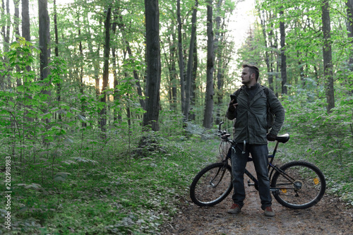 Young man with backpack and glasses standing with bicycle on the forest path of the park and looking, active lifestyle concept, sport and jorney, travel surviver concept