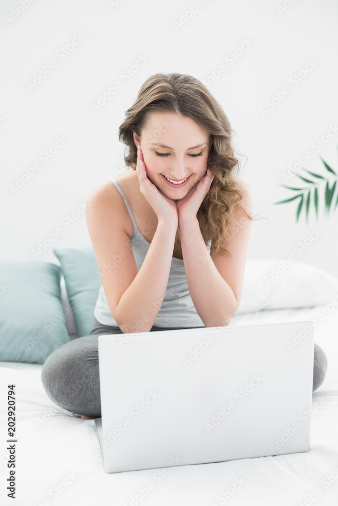 Smiling casual brunette looking at laptop in bed Smiling casual brunette looking at laptop in bed