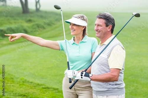 Golfing couple smiling and holding clubs 