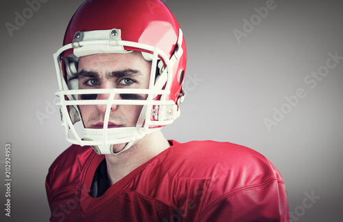 Portrait of a serious american football player taking his helmet looking at camera against grey vignette