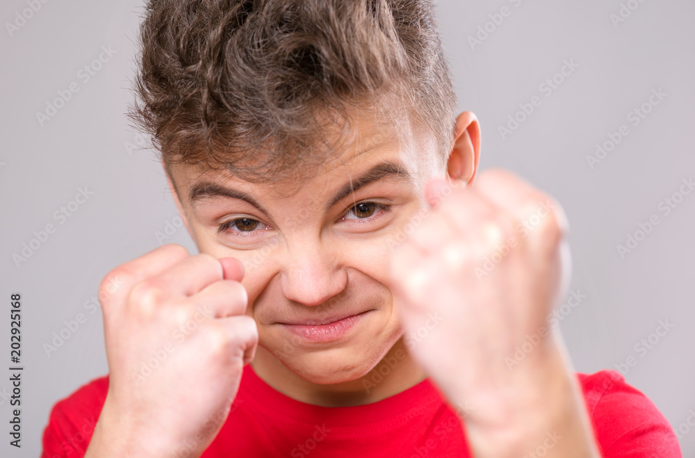 Emotional portrait of irritated teen boy. Furious teenager looking with anger at camera. Handsome outraged child threatens with a fist, isolated on white background. Emotional portrait of irritated teen boy. Furious teenager looking with anger at camera. Handsome outraged child threatens with a fist, isolated on white background.