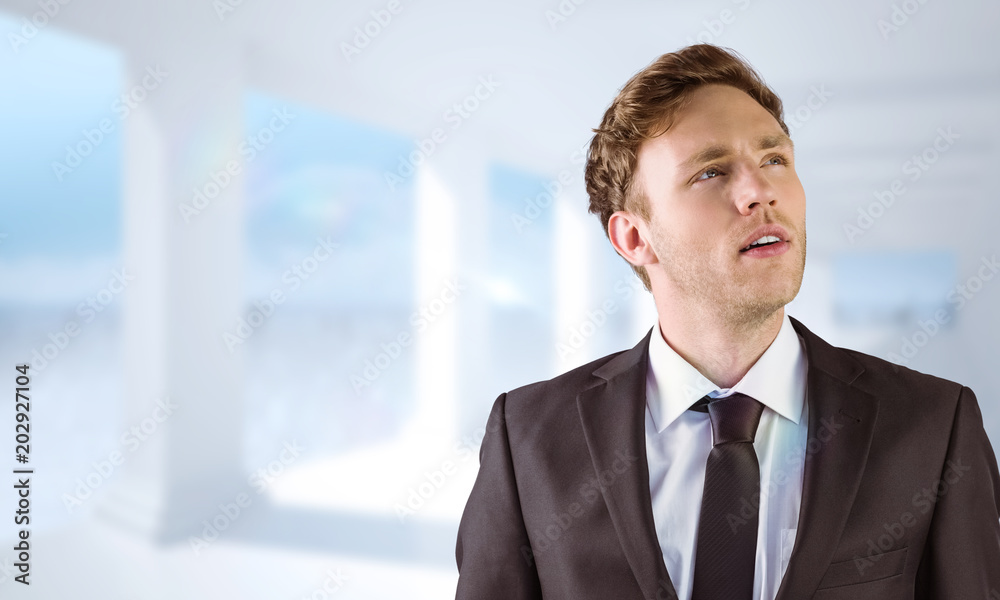 Young businessman thinking and looking up against bright white room with columns Young businessman thinking and looking up against bright white room with columns