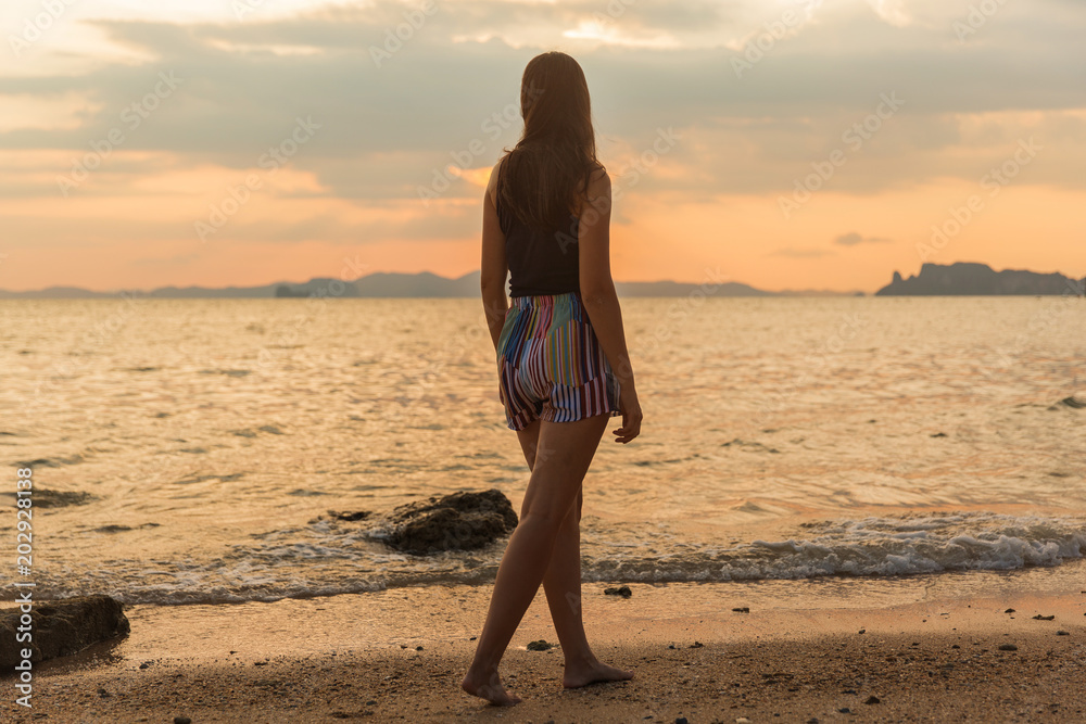 Young fit sexy girl in standing on a beach during sunrise or sunset in  front of a calm sea, showing back to the camera. Stock Photo | Adobe Stock