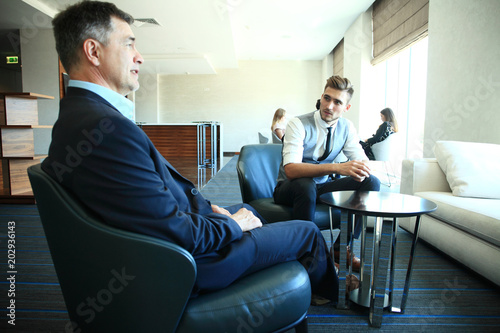 Mature businessman using a digital tablet to discuss information with a younger colleague in a modern business lounge.