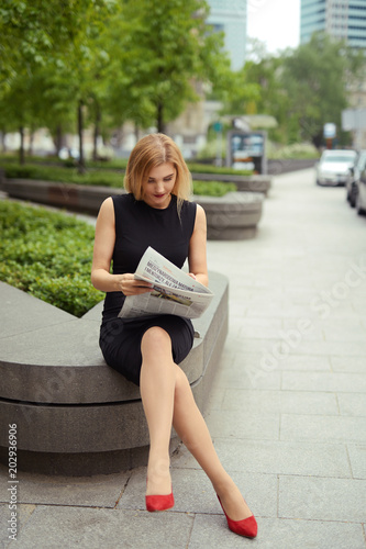 Smart blonde girl sitting with newspaper and read