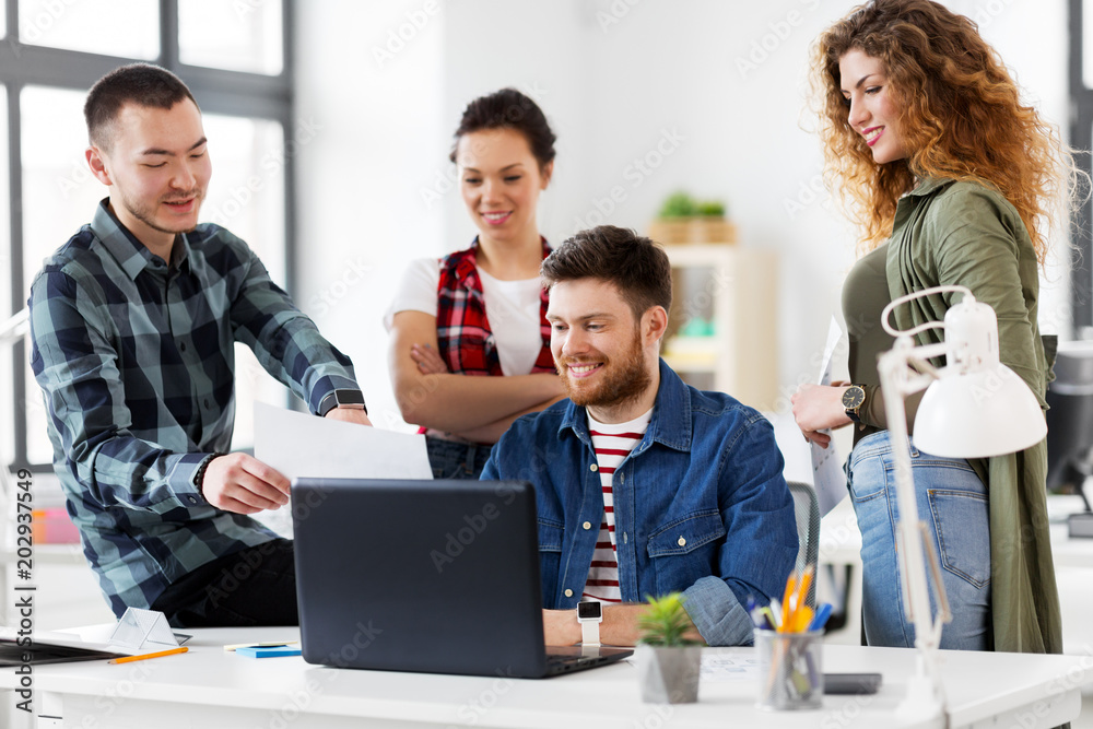 business, technology and people concept - happy creative team with laptop computer and papers working at office business, technology and people concept - happy creative team with laptop computer and papers working at office
