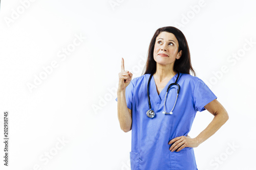 Portrait of a female doctor in blue uniform pointing and looking up, isolated on white studio background