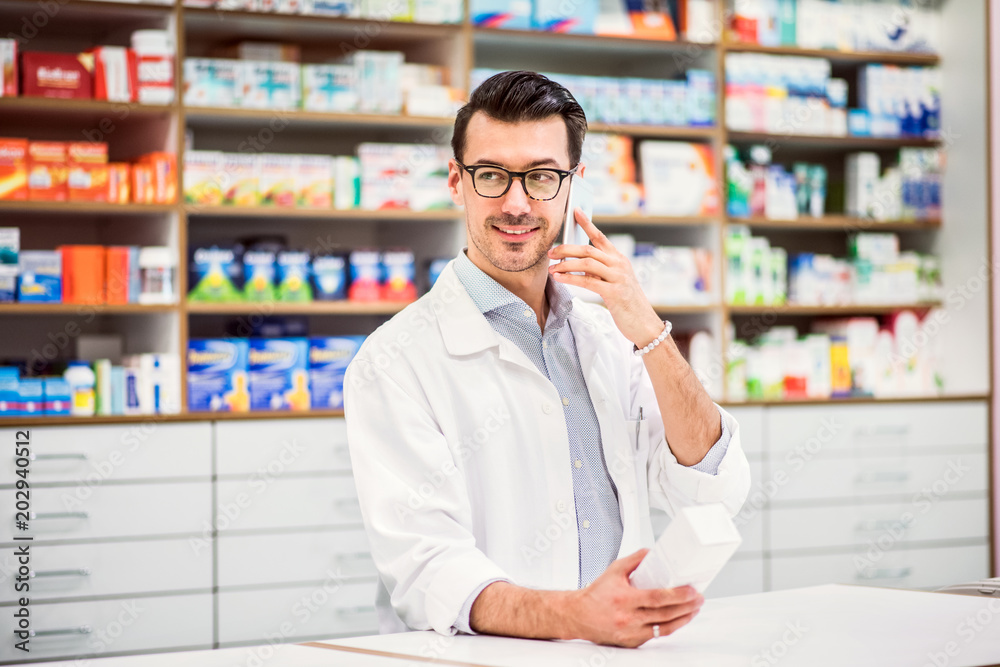 Young friendly male pharmacist with smartphone, making a phone call.