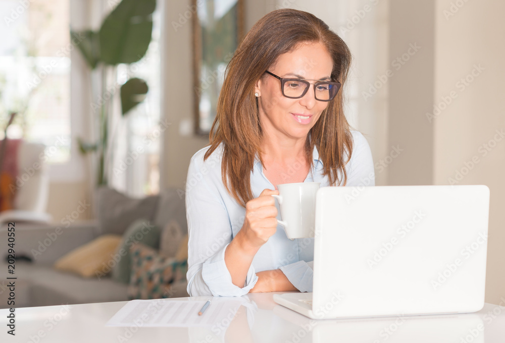 Middle age woman using computer and drinking coffee, indoor Middle age woman using computer and drinking coffee, indoor