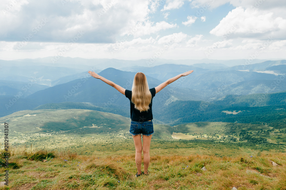 Young girl relaxing and enjoying scenic view on top of mountain. Bliss and happiness. Beautiful summer nature landscape. Lonely young blonde teen traveler dreaming outdoor on vacation. Romantic mood Young girl relaxing and enjoying scenic view on top of mountain. Bliss and happiness. Beautiful summer nature landscape. Lonely young blonde teen traveler dreaming outdoor on vacation. Romantic mood