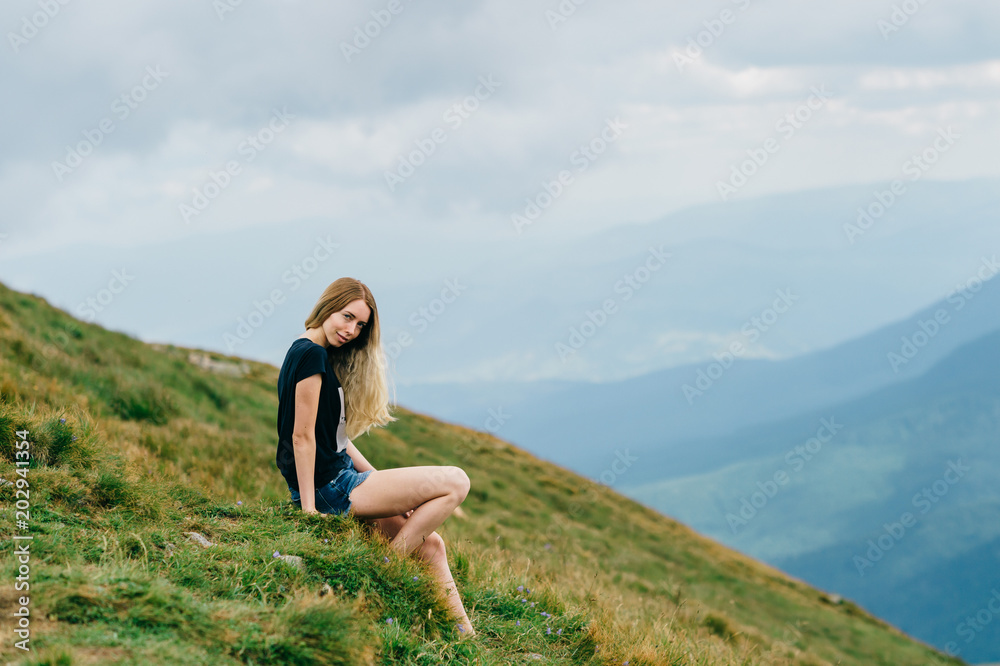 Young girl relaxing and enjoying scenic view on top of mountain.  Bliss and happiness. Beautiful summer nature landscape. Lonely young blonde teen traveler dreaming outdoor on vacation.  Romantic mood