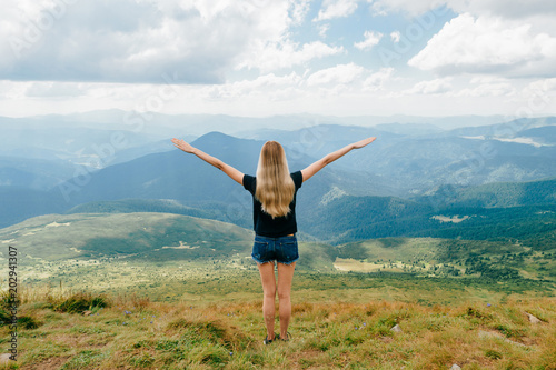 Young girl relaxing and enjoying scenic view on top of mountain. Bliss and happiness. Beautiful summer nature landscape. Lonely young blonde teen traveler dreaming outdoor on vacation. Romantic mood