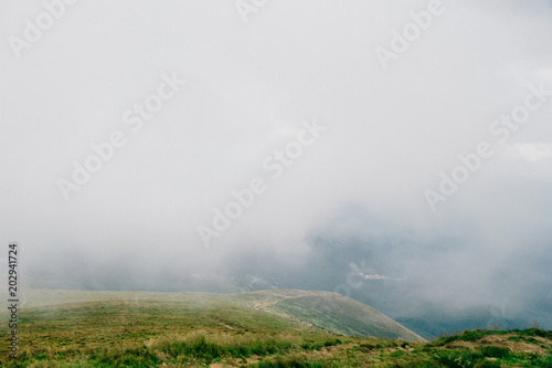 Foggy weather in mountains. Travelers hiking over misty hiils. Tourists climbing up. Healthy activity. Summer moody scenic view from high altitude at nature outdoor. Beauftiful landscape. Trekking.
