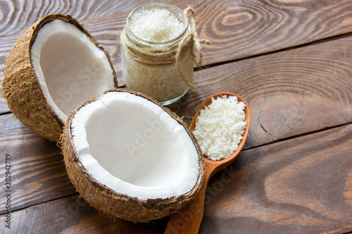 fresh coconut cracked in half on a wooden table with coconut chips in a glass jar and in a wooden spoon with a place for writing