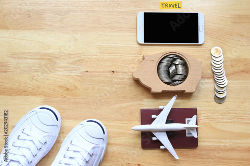 Saving planning for Travel budget of holiday concept, White sneakers shoes and airplane on passport with a smartphone and stack of coins money in piggy bank wood on the table background photo