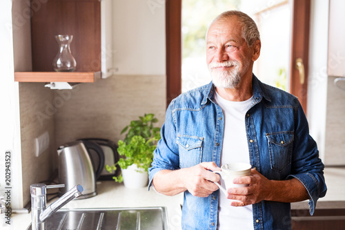 Happy senior man holding a cup of coffee in the kitchen.