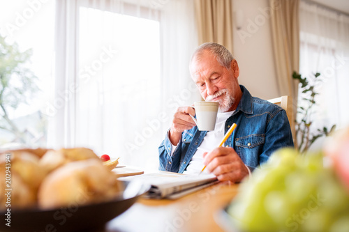 Senior man eating breakfast and doing crosswords at home. photo