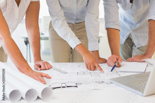 Mid section of business people working on blueprints at office
