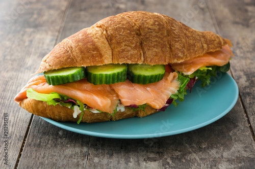 Croissant sandwich with salmon and vegetables on wooden table