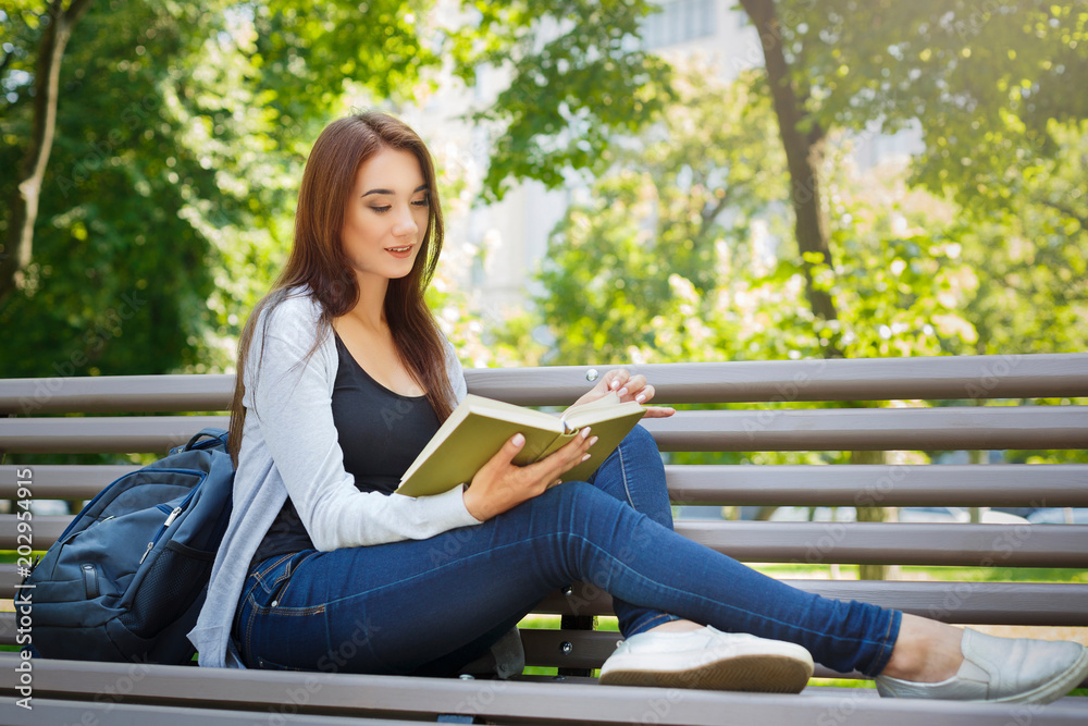 Young asian woman sitting on a bench in the park. Relaxing and reading a book Young asian woman sitting on a bench in the park. Relaxing and reading a book