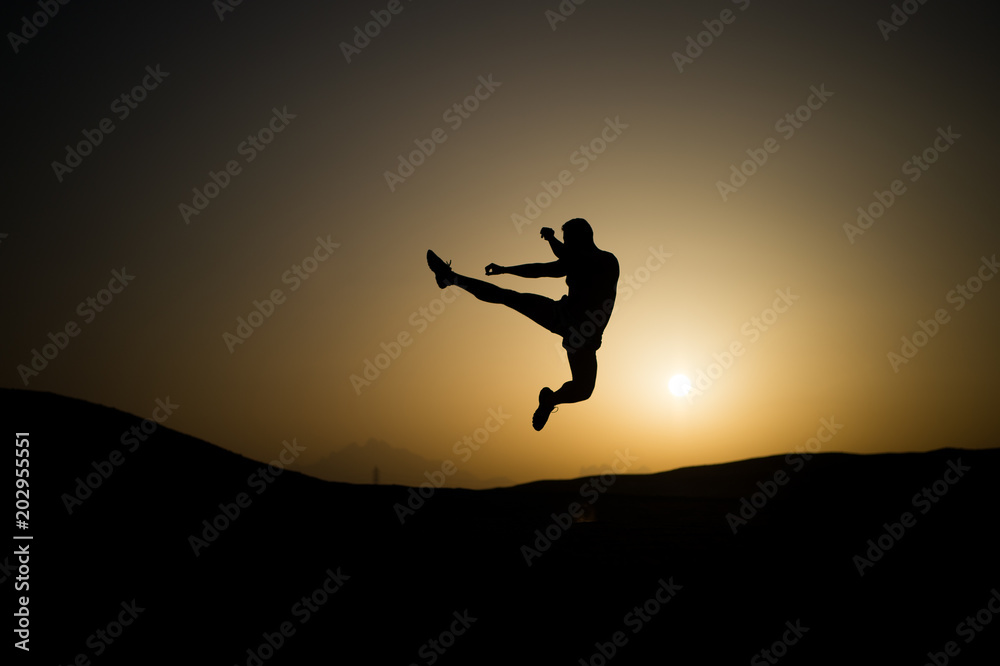 Athlete jump high with energy. Sportsman silhouette on sunset sky. Man training on natural landscape. Workout in summer dusk. Sport, wellness and bodycare concept