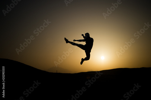 Athlete jump high with energy. Sportsman silhouette on sunset sky. Man training on natural landscape. Workout in summer dusk. Sport, wellness and bodycare concept