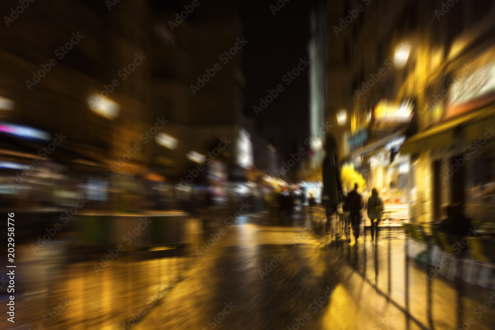 Blurry motion image of people walking on street at night in Paris.