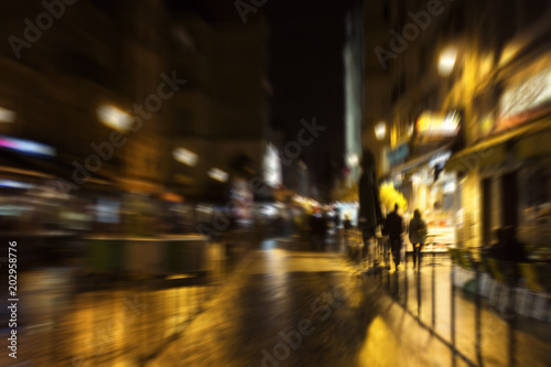 Blurry motion image of people walking on street at night in Paris.