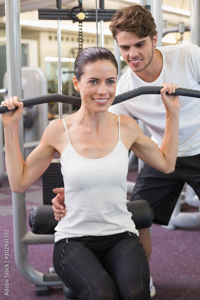 Fit brunette using weights machine for arms with trainer helping