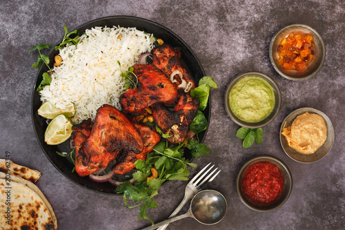 Tandoori chicken wings with spicy pilau rice, lime and traditional assortment of sauces on rustic table, top view photo