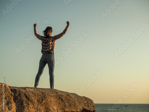 Φωτογραφία triumphant WOMAN IN YES POSE WITH arms wide open on top of a rock at the beach