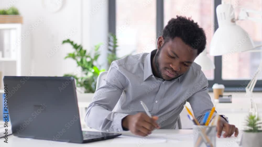 business, people, paperwork and technology concept - african american businessman with laptop computer and papers working at office business, people, paperwork and technology concept - african american businessman with laptop computer and papers working at office