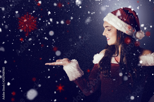 Pretty girl in santa costume holding hand out against snow