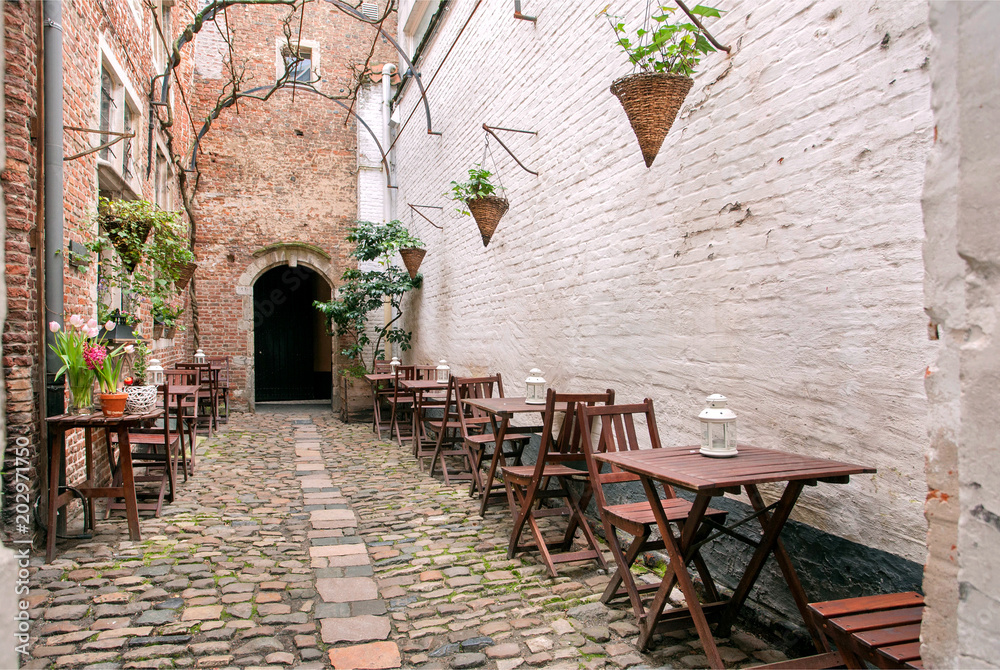 Small outdoor cafe in old style narrow street with brick walls, wooden furniture and cobbled stones.
