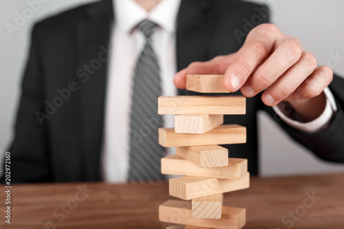Businessman placing wooden block on a tower. Planning, risk and business strategy concepts.
