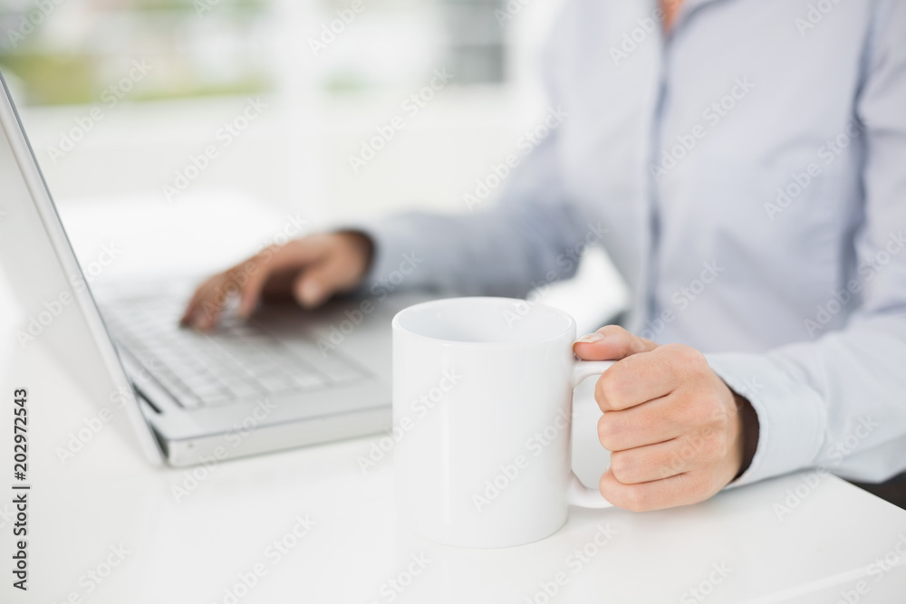 Mid section of a businesswoman using laptop while having coffee Mid section of a businesswoman using laptop while having coffee