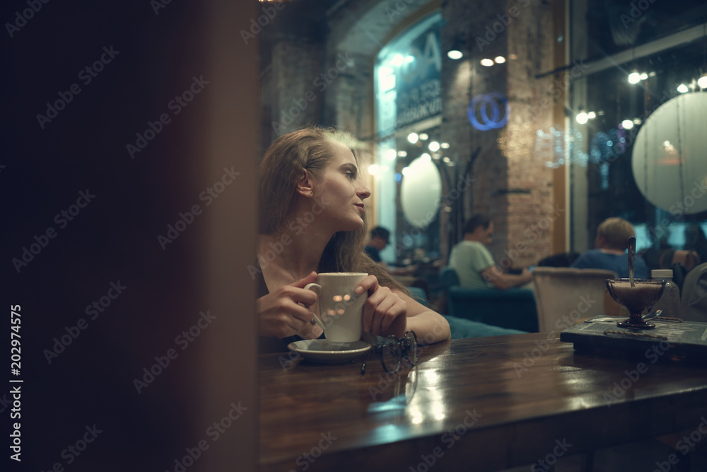 girl sitting in a cafe for a cup of coffee. Young lady looks out the window in a restaurant