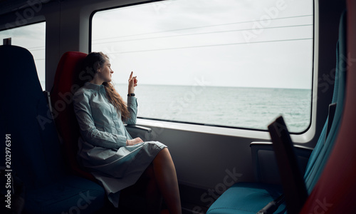 Thoughtful girl was going home on the train. Beautiful view from the train window to the sea. The girl points to the sea